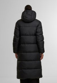 Svart puffjacka med huva, med en lång, vadderad design och en slät yta. Jackan når till mitten av vadbenen med en figursydd silhuett.