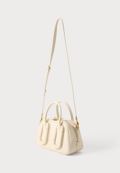 Sac à main en cuir couleur crème avec poignées arrondies et bandoulière longue réglable, doté de fermetures éclair et de pièces en métal doré, présenté sur fond blanc.