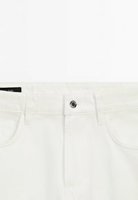Section de la taille d'un jean en denim blanc avec bouton frontal, passants pour ceinture et poches avant visibles.