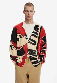 Knit cardigan featuring red, cream, and black colors, adorned with a Mickey Mouse graphic and text. It has a button front and loose fit.