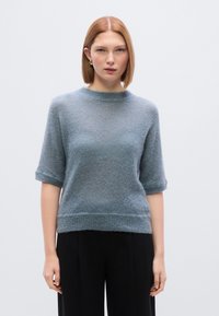 Ανοιχτό μπλε, πλεκτό πουλόβερ με κοντά μανίκια, στρογγυλή λαιμόκοψη και ριμπ τελείωμα. Μαλακή υφή, άνετη εφαρμογή και ρεβέρ στα μανίκια.