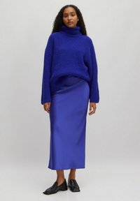Oversized cobalt blue sweater with a high turtleneck, paired with a sleek satin cobalt blue midi skirt and black slip-on shoes.