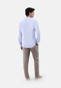 Hellblaues Hemd mit langen Ärmeln, geknüpften Manschetten und geradem Schnitt, kombiniert mit beigefarbenen, strukturierten Hose und hellen Sneakers.