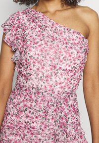 Robe fleurie à une épaule avec des volants superposés, présentant des fleurs roses et grises sur un fond clair, et un détail à nouer à la taille.