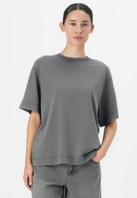 Grijze oversized t-shirt van een katoenmix stof, ronde halslijn, korte mouwen en rechte zoom. Gedragen met bijpassende grijze broek.