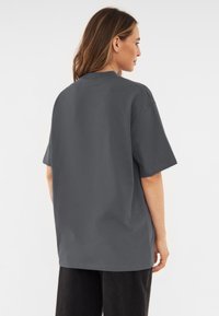 Szara, oversize koszulka z krótkim rękawem, okrągłym dekoltem i miękką teksturą, w połączeniu z czarnymi spodniami o luźnym kroju.