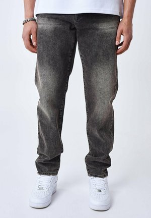 Jeans in denim nero con lavaggio sbiadito, taglio dritto, tasche frontali e una leggera texture abrasata, indossati con sneakers bianche.