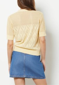 Jasnożółty, dzianinowy sweter z krótkimi rękawami, zdobiony wzorem w romby i ściągaczem u dołu, zestawiony z niebieską dżinsową spódnicą.