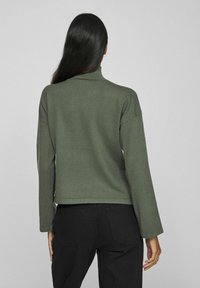 Olive rohelise värvi kõrge kaelusega pullover, millel on langenud õlad, soonikkoes krae ja lühendatud lõige. Pehme tekstuur ja minimalistlik disain.