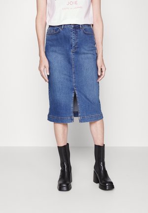 Dżinsowa spódnica midi z przednim rozcięciem, klasyczne niebieskie pranie, z surowym wykończeniem na dole, noszona z czarnymi botkami na obcasie.