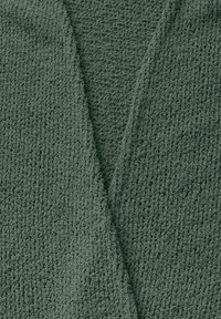 Tissu vert mousse texturé avec un tissage lâche. Le design présente un décolleté en V et des sections superposées, soulignant la douceur et la chaleur.