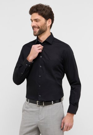 Schwarzes Langarmhemd mit Knopfkragen, Brusttasche, glatter Textur und passenden Knöpfen, getragen mit grauen Hosen und einem schwarzen Gürtel.