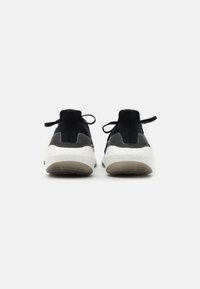 Zapatillas deportivas negras con parte superior de tejido texturizado, entresuela blanca y suela de goma. Las características incluyen cordones y asas en el talón.