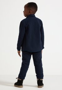 Navy blue fleece outfit with a collar and long sleeves, featuring tapered pants and contrasting cuffs. Black boots with fur trim.
