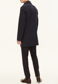 Marinkapp med skräddarsydd passform, med hög krage, rak skärning och knappade manschetter. Slätt tyg, bärs med mörka byxor och skor.