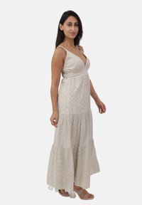 Abito maxi beige chiaro con scollatura a V profonda, corpino aderente e gonna a balze. Il tessuto testurizzato presenta piccoli punti decorativi.