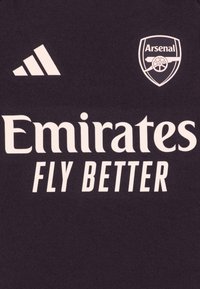 Maillot de sport noir avec le logo Adidas blanc, l'emblème d'Arsenal et le texte "Emirates FLY BETTER" imprimé de manière proéminente sur le devant.