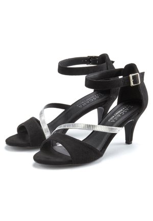 Schwarze Wildleder-High-Heelsandalen mit silbernen Kreuzriemen, offener Zehenbereich und Knöchelriemen, der mit einer Schnalle gesichert ist.