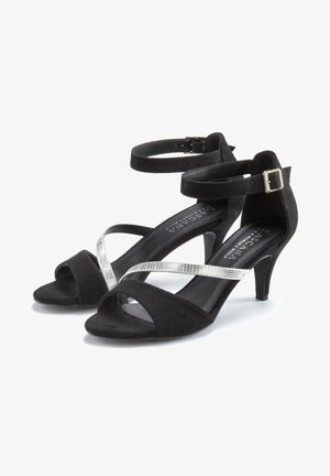 Schwarze Wildleder-High-Heelsandalen mit silbernen Kreuzriemen, offener Zehenbereich und Knöchelriemen, der mit einer Schnalle gesichert ist.