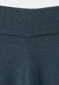 Gros plan sur un tissu tricoté bleu foncé avec une ceinture côtelée et un détail de couture centrale.