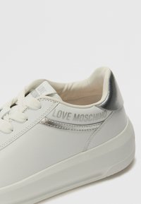 Sneaker in pelle bianca con dettagli argento, logo sul tallone, punta rotonda e suola piatta, caratterizzato da chiusura con lacci e interno imbottito.