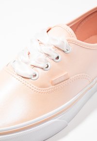 Sneaker wykonany z brzoskwiniowej skóry, z białymi satynowymi sznurowadłami, przeszyciami i gumową podeszwą. Po stronie znajduje się metka z logo Vans.