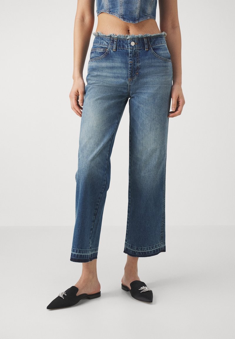 Jeans larges taille haute bleu clair avec ourlet effiloché. Design à cinq poches, fermeture à bouton, fabriqués en denim, assortis à des chaussures noires à enfiler.