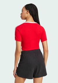 Red cropped t-shirt with short sleeves and white accents; paired with black ribbed shorts featuring an elastic waistband.