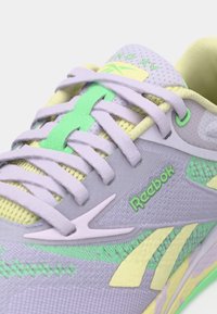 Adidaș violet cu accente galbene deschise și verzi, având material din plasă, șireturi, logo pe lateral și detalii texturate.