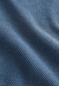 Sinine kangas tekstuurse vahvlilõnga mustriga, millel on pehmed voldid ja varjud, mis viitavad paindlikule materjalile.