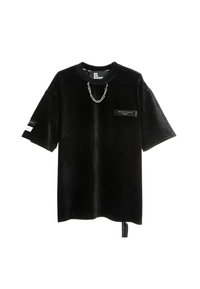 Camisa negra de gran tamaño hecha de pana, con mangas cortas, un acento de cadena y un bolsillo frontal con una etiqueta rectangular.