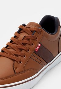 Bruna lädersneakers med bruna detaljer, texturerad sidopanel, vit gummisula och bruna snörningar. Liten röd Levi's-logotyp på sidan.