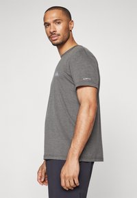 Camiseta gris de manga corta en un tejido suave y ligero, con un pequeño logo en el pecho y un acento "DRYFLIGHT" en la manga.