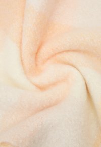 Pehmeane, tekstuuriline kangas pastelloranžis ja kreemis, õrnalt keerdus, et näidata selle gradientset värvi ja pehmet tunnet. Pole silmapaistvaid mustreid ega aksessuaare.