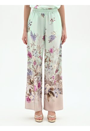 Donna che indossa pantaloni a gamba larga con stampa floreale pastello e vita elastica, abbinati a sandali con plateau aperti in oro.