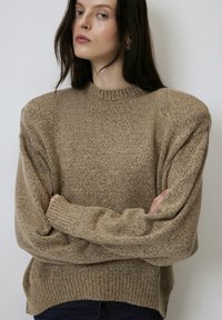 Maglione lavorato a maglia beige con un motivo texturizzato e macchiato, scollo rotondo e spalle scese. Polsini e orlo a coste.