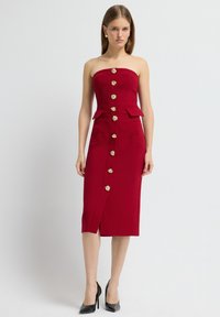 Rode strapless midi-jurk met een aansluitend lijfje, gouden knopen aan de voorkant en twee voorzakken; heeft een zijsplit en peplumdetails.