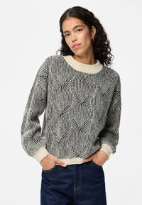 Texturiertes Sweatshirt in Schwarz und Creme mit einem geometrischen Blattmuster, ausgestattet mit einem gerippten Rundhalsausschnitt und gekrempelten Ärmeln.
