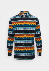 Hemd mit Knopfleiste, das ein mehrfarbiges Zickzack- und Dreiecksmuster zeigt. Hergestellt aus einem Stoff mit weicher Textur. Die Farben umfassen Marineblau, Gelb und Rot.