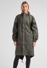 Gabardina larga de color verde oliva con capucha, cremallera frontal, cinturilla elástica y un parche negro en la manga; cuenta con un dobladillo ajustable.