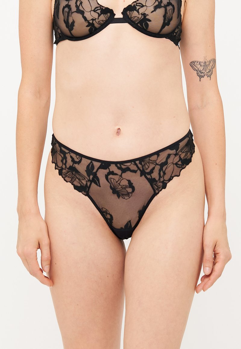 Black lace bra and matching thong featuring floral patterns, sheer material, scalloped edges, and thin straps. Elegant design with detailed accents.