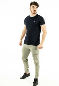 Camiseta azul marino con ribete blanco, de mangas cortas y logo en el pecho, combinada con pantalones cargo caquis y zapatillas negras.