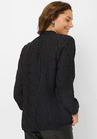 Black long-sleeve blouse featuring a textured wave pattern, loose fit, and a round neckline, seen from the back.