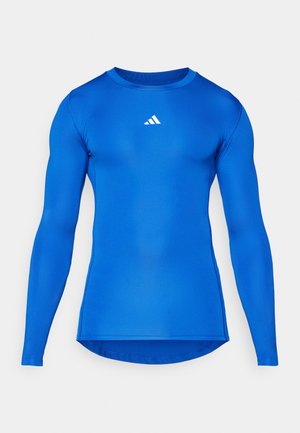 Langermet treningsskjorte i ensfarget blå, laget av elastisk stoff. Har rund hals og en liten hvit logo på brystet.