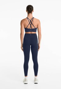 Soutien-gorge de sport bleu marine avec des bretelles croisées, associé à un legging taille haute. Les deux articles présentent une texture lisse et extensible.