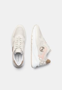 Zapatillas beige con materiales de malla y cuero. Presentan acentos rosas y detalles en un tono beige con patrón. Suela blanca gruesa para mayor amortiguación.