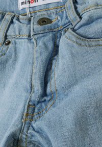 Svijetloplava traper tkanina s vidljivim šavovima, metalnim gumbom i detaljima prednjeg džepa, prikazuje dizajn ležernih hlača.