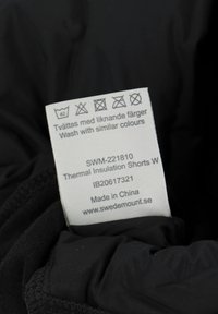 Black thermal insulation shorts with a care label, displaying symbols and text, made of woven fabric. Label includes brand and washing instructions.