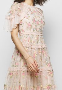 Robe en tissu rose transparent avec broderies florales, présentant des manches à volants, une structure en étages et des motifs floraux pastel intricats.