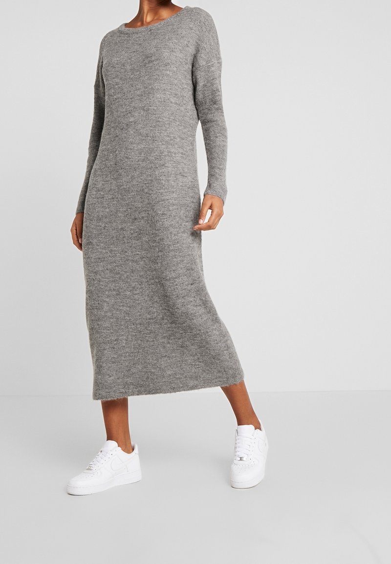 Lång, grå stickad klänning med båturringning och långa ärmar, i kombination med vita sneakers. Texturen är mjuk och något fluffig.